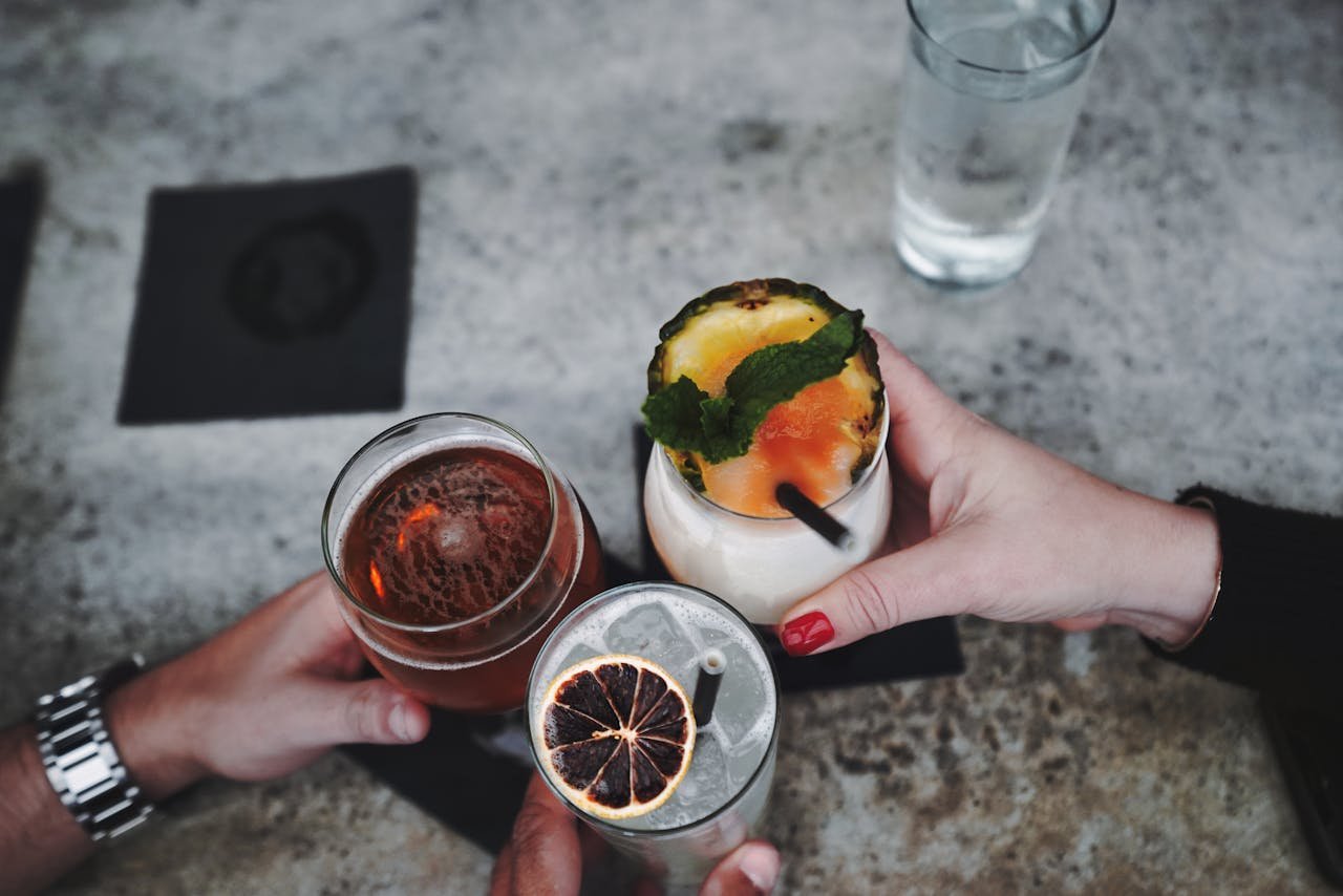 services-04 Close-up of hands holding and clinking various cocktails and drinks over a table.
